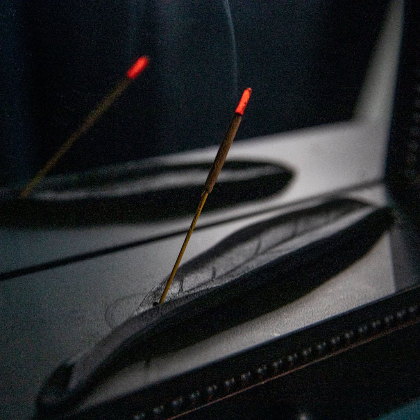 A black leaf-shaped incense burner with a few incense sticks placed in it, glowing with a warm light, set on a flat surface.