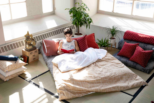 Man laying in a floor futon, surrounded by plants, statues and a tatami floor.