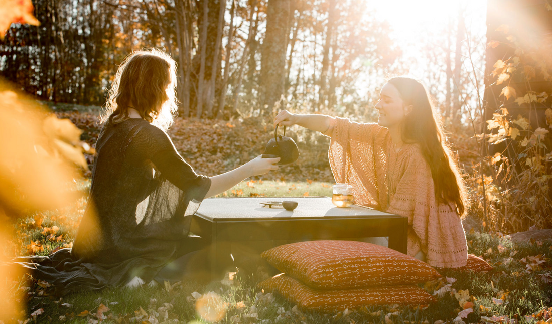 two woman pouring tea outside on an autumn day with a floor table and tea set with zabutons