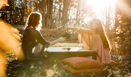 two woman pouring tea outside on an autumn day with a floor table and tea set with zabutons