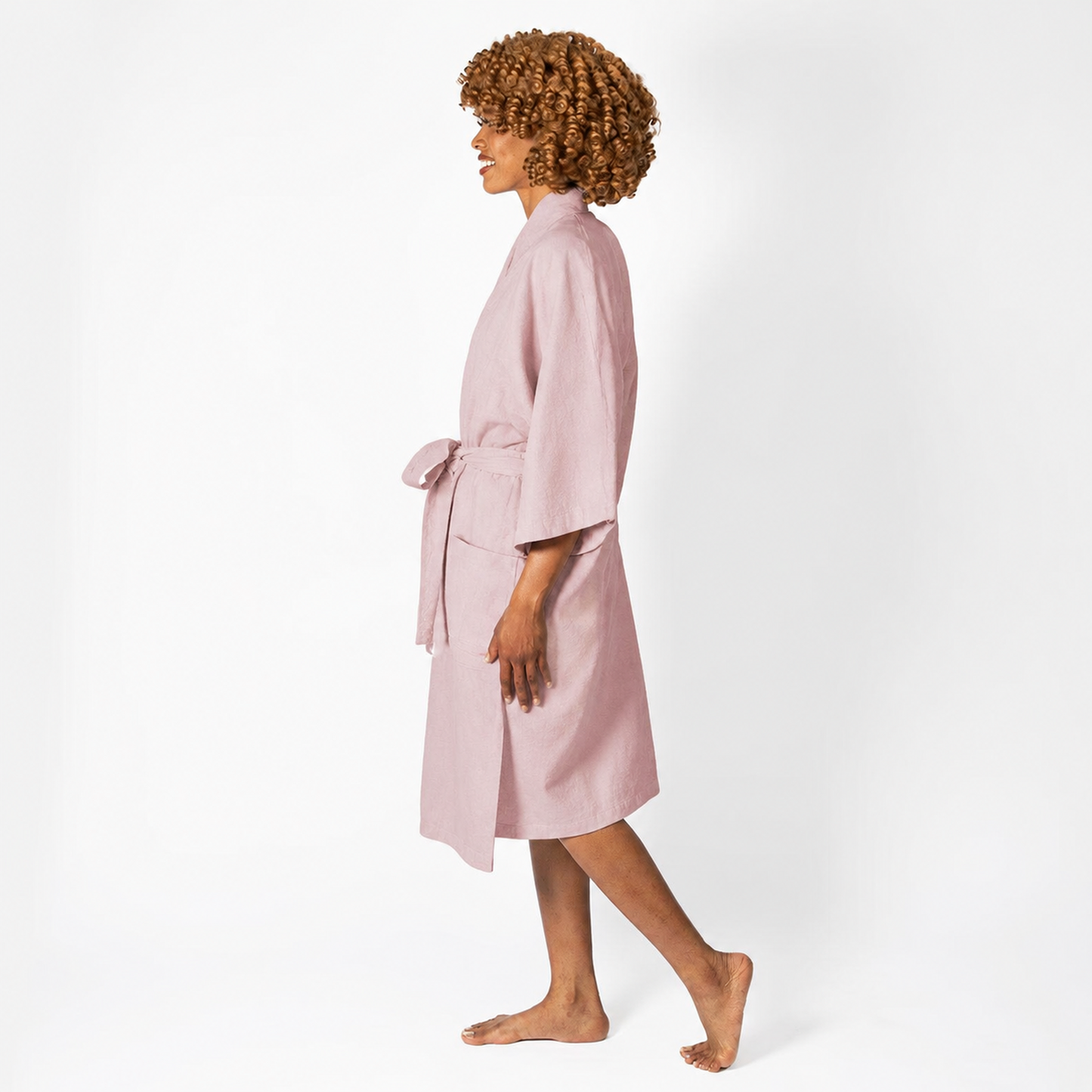 A woman wearing a light pink cotton robe, shown in profile against a plain white studio background.