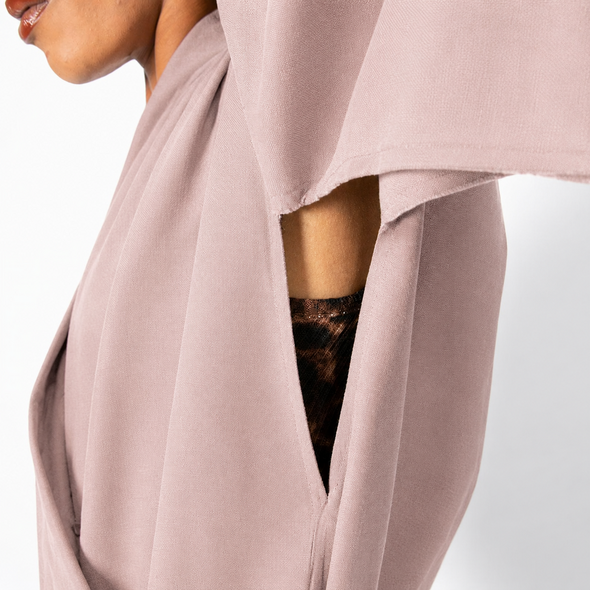 A close-up of a model wearing a dusty pink draped wrap top with a side slit showing a black lace underlayer, against a clean white background.