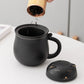 Person pouring tea into a black mug with a bamboo tea infuser, on a light gray background.