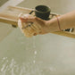 Hand holding a bath pouf over a bathtub with water flowing.
