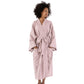 A woman wearing a light pink cotton bathrobe with a tie belt, standing against a plain white studio background.