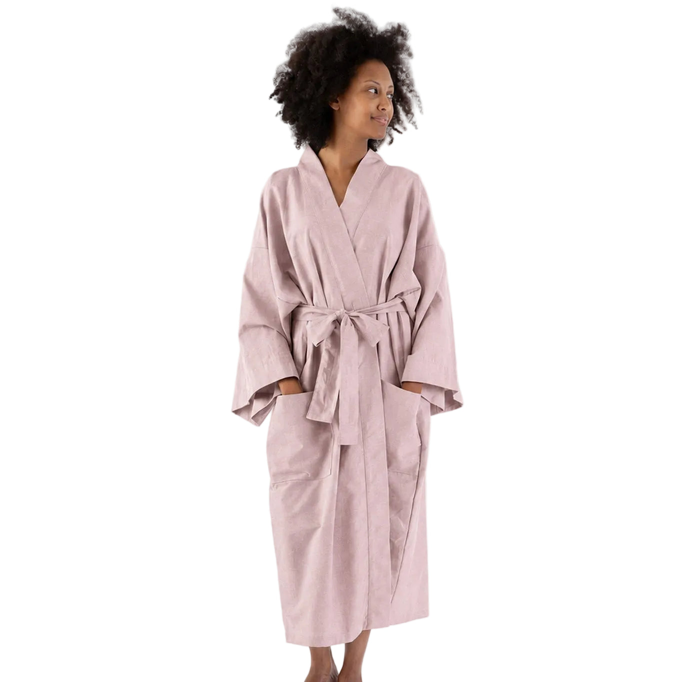 A woman wearing a light pink cotton bathrobe with a tie belt, standing against a plain white studio background.