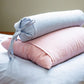 Two rolled-up pillows, one light blue and one pink, on a bed.