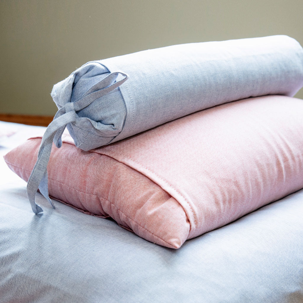 Two rolled-up pillows, one light blue and one pink, on a bed.
