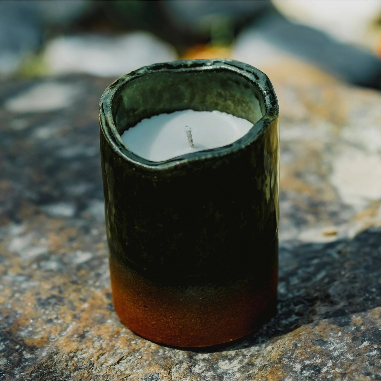 Candle in a green ceramic holder on a rocky surface