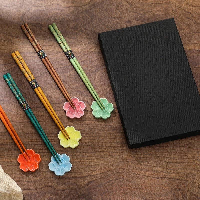 Set of colorful chopsticks with floral ends on a wooden surface next to a black giftbox.