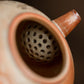 Close-up of a ceramic tea strainer with a brown background