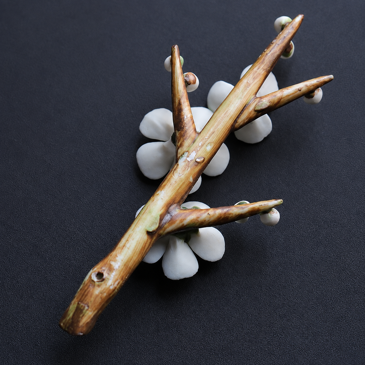 A decorative branch-shaped incense holder with white flower petals and small buds, photographed on a dark textured background.