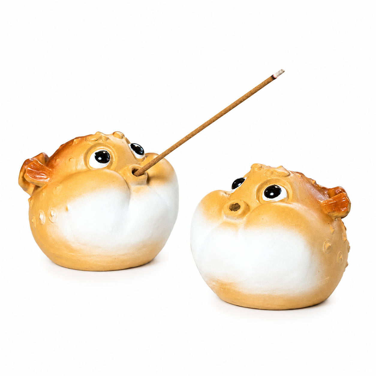 Two puffer fish-shaped ceramic incense holders on a white background, one holding a wooden incense stick.