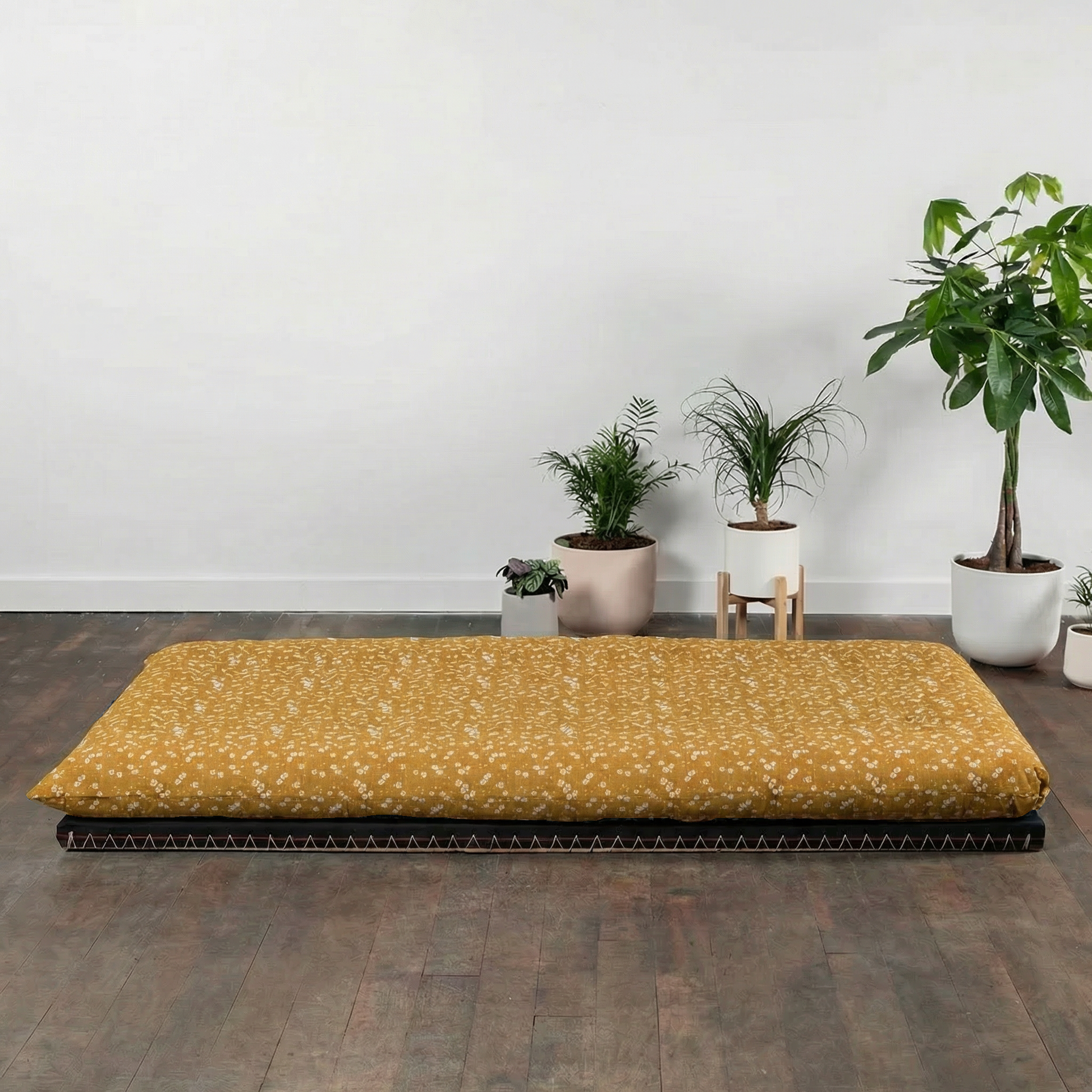 Yellow mattress on a wooden floor with potted plants in the background