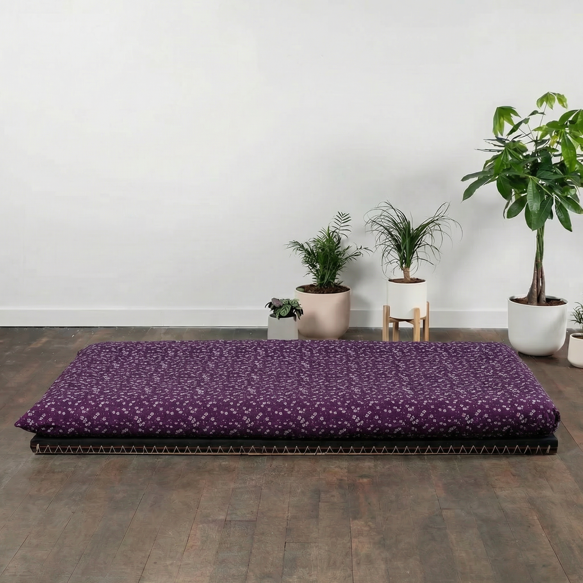 Purple mattress on a wooden floor with potted plants in the background