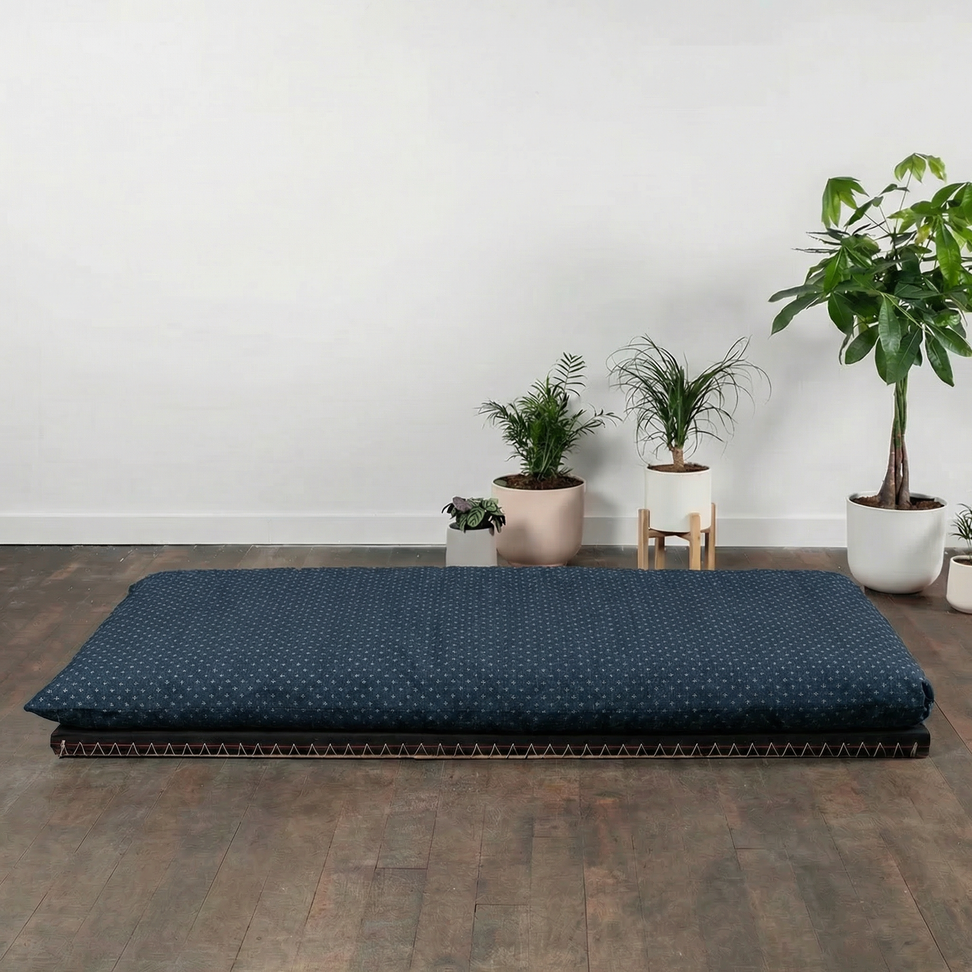 Blue mattress on a wooden floor with potted plants in the background