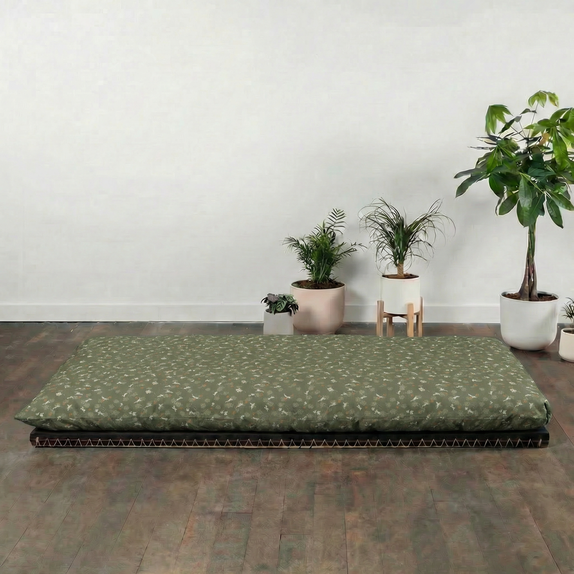 Green futon mattress on a wooden floor with potted plants in the background