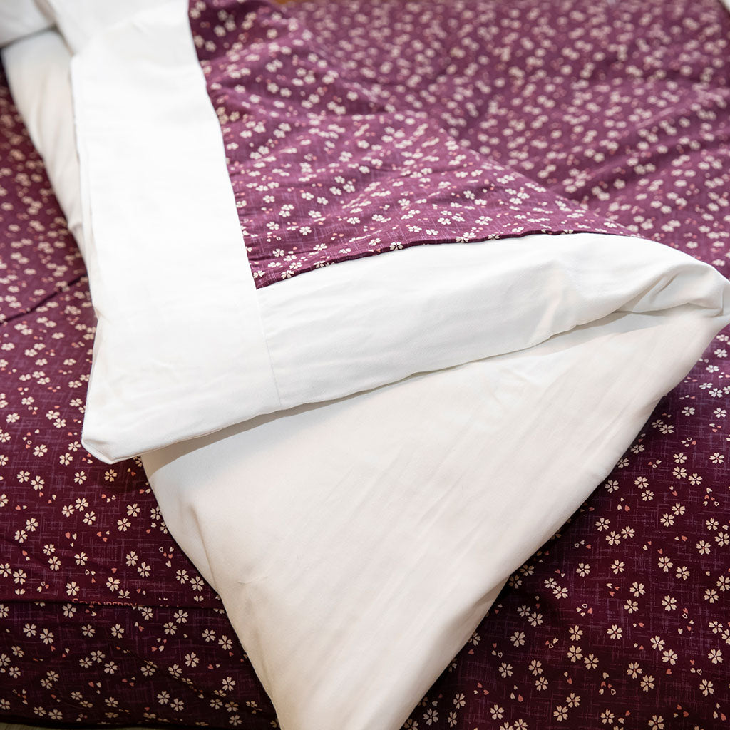 A traditional Japanese kakefuton comforter in purple with a white border, displayed on a bed.