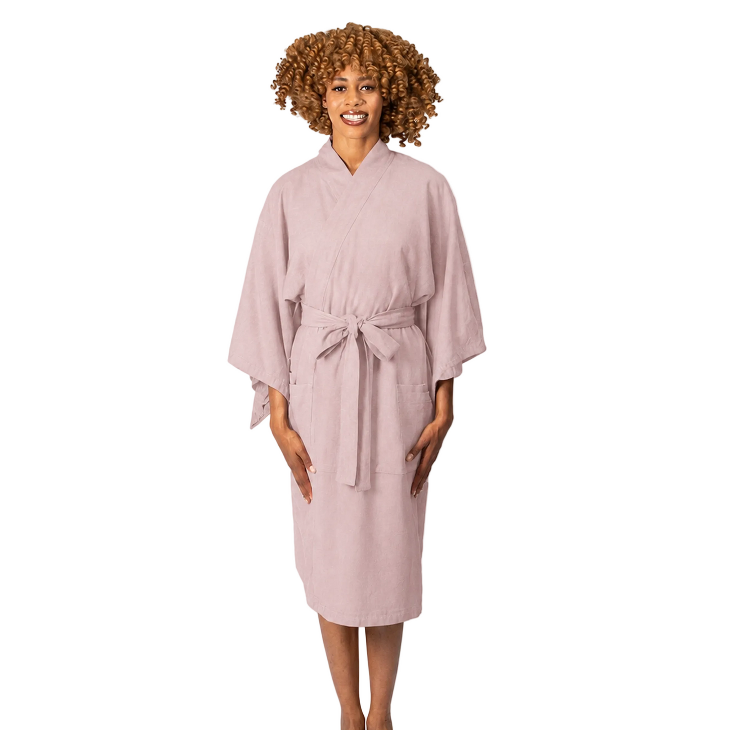 A woman wearing a dusty pink cotton robe with a tie belt, standing against a plain white studio background.