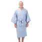 A smiling older man wearing a light blue kimono-style bathrobe with a tie belt, standing barefoot against a plain white studio background.