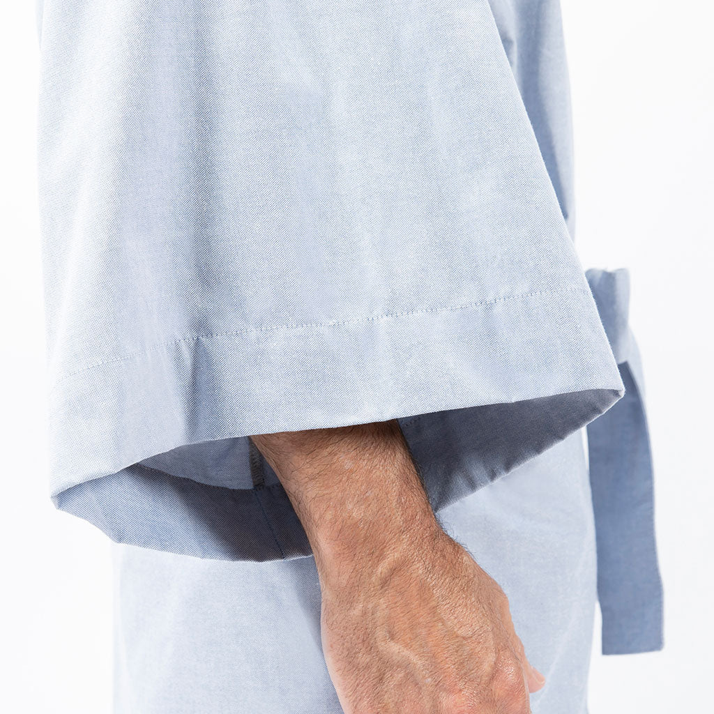 Close-up of a person wearing a light blue kimono-style robe, showing the wide sleeve cuff and part of the arm against a plain white background.
