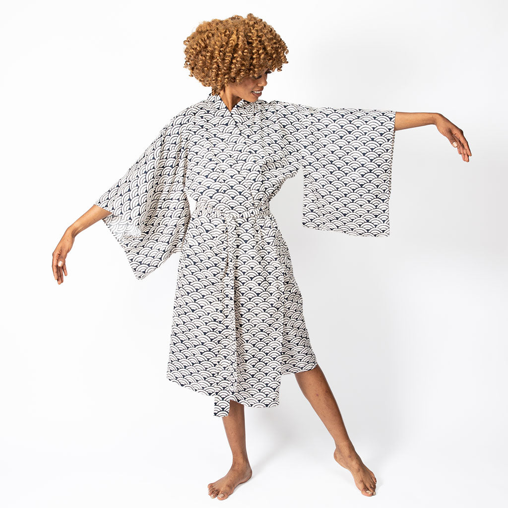 A woman modeling a white kimono-style robe with a black geometric pattern, featuring wide bell sleeves and a self-tie waist, set against a plain white studio background.