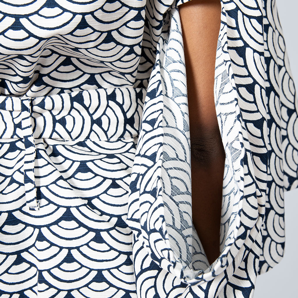 Close-up of a navy blue and white scallop patterned garment with a tie detail and a visible arm opening.