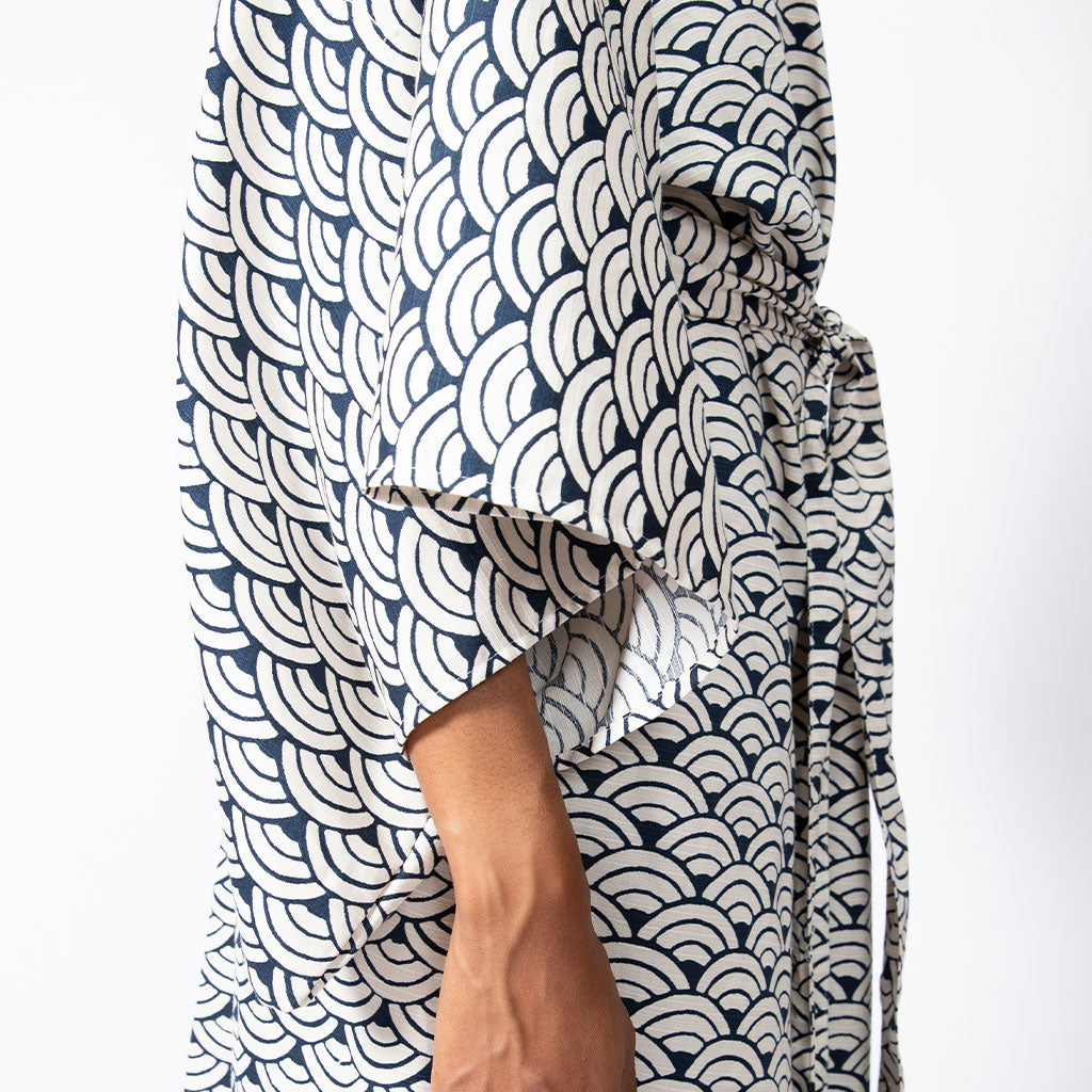 A close-up of a person wearing a loose, short-sleeved kaftan-style top with a navy blue and off-white scallop pattern, tied at the waist.