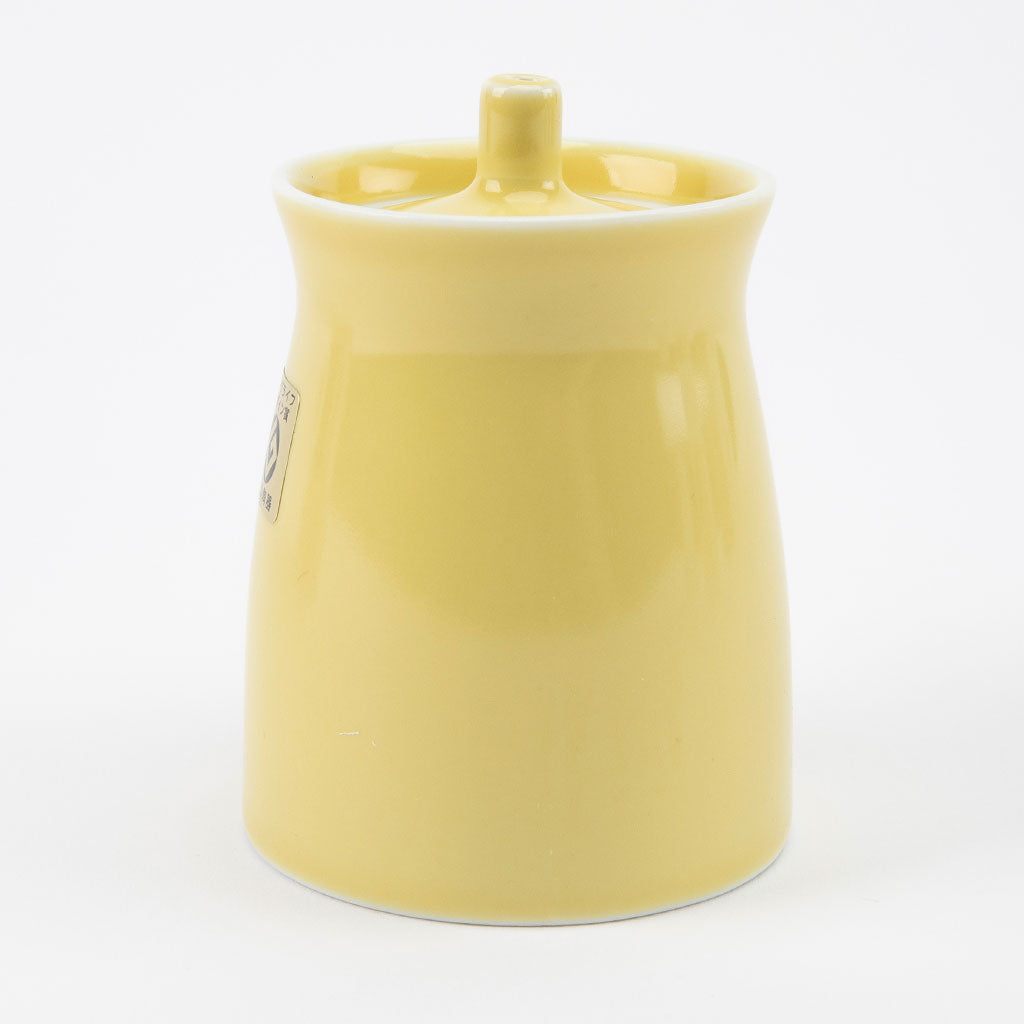 Yellow ceramic soy sauce dispenser with a handle on a white background