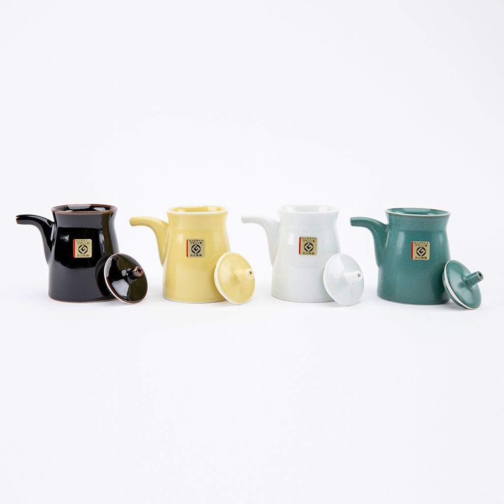 Four ceramic soy sauce dispensers in black, yellow, white, and green on a white background