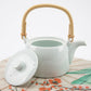 White ceramic teapot with a bamboo handle on a floral-patterned surface