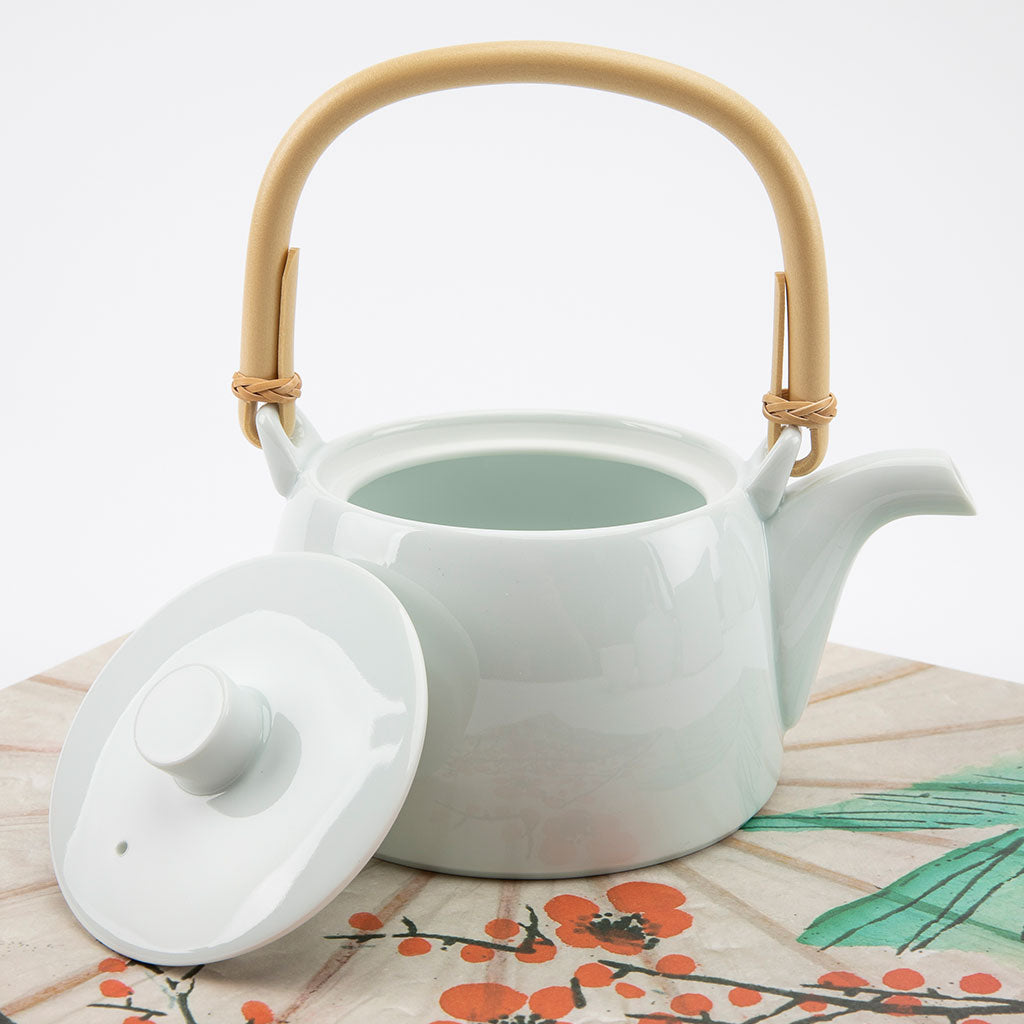 White ceramic teapot with a bamboo handle on a floral-patterned surface