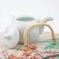 White ceramic teapot with a bamboo handle on a floral-patterned surface