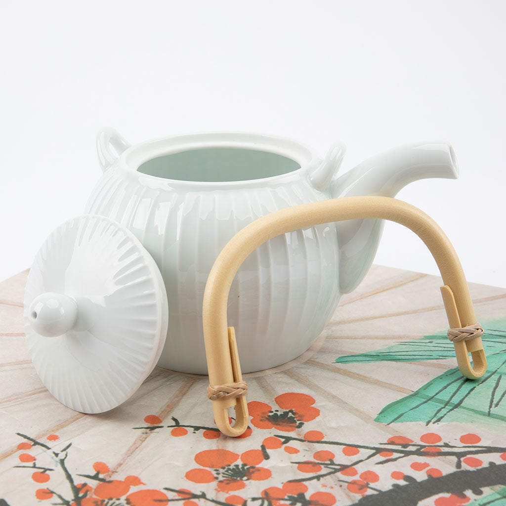 White ceramic teapot with a bamboo handle on a floral-patterned surface