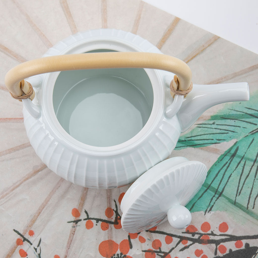 White ceramic teapot with a beige handle on a decorative surface with floral patterns.