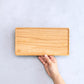 Wooden cutting board held by a hand on a light gray background
