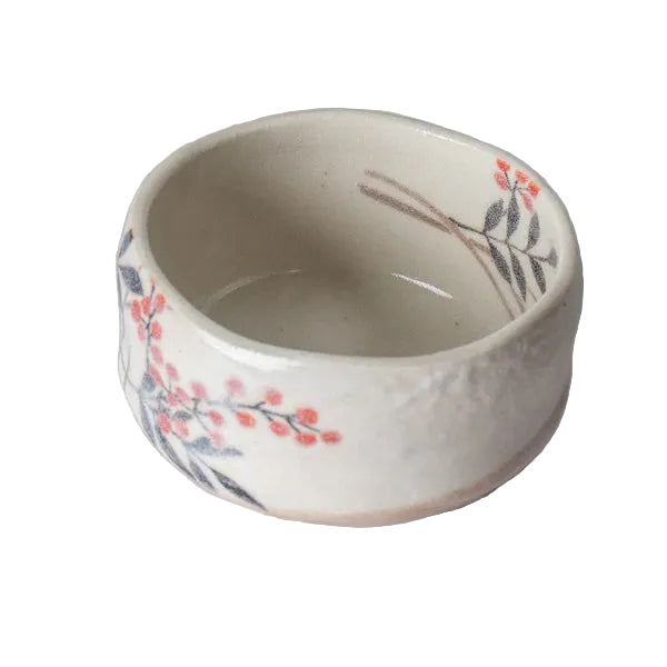 A small round ceramic bowl with a textured off-white glaze, decorated with delicate hand-painted cherry blossom branches in red and gray, resting on a light gray marble surface.