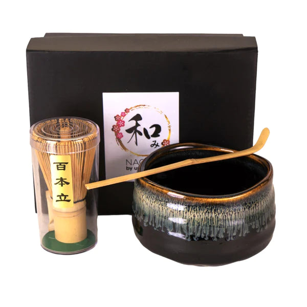 Matcha set including black box, bamboo whisk, spoon and black bowl on a white background.
