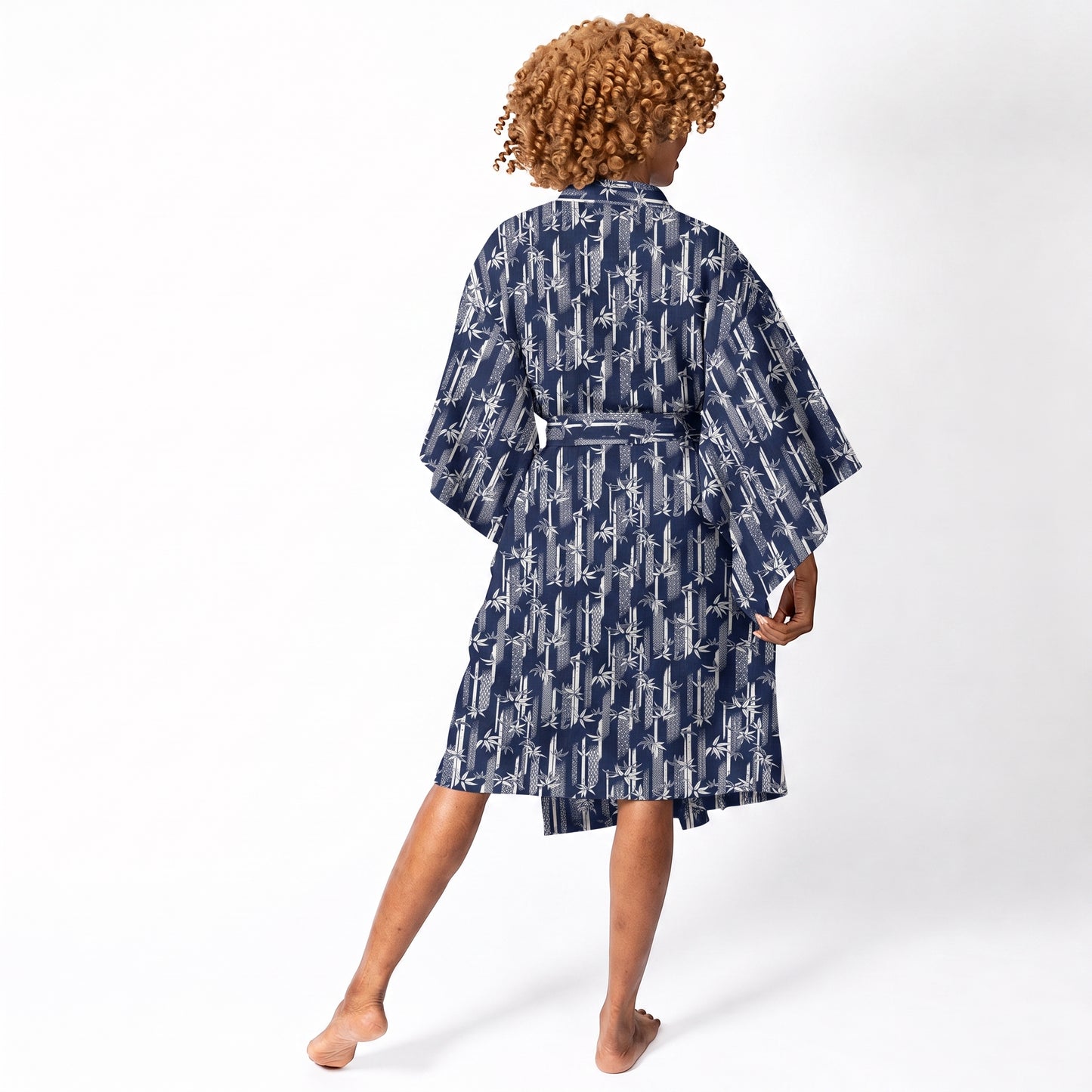 A woman shown from the back wearing a navy blue kimono-style robe with a white abstract pattern, standing against a plain white studio background.