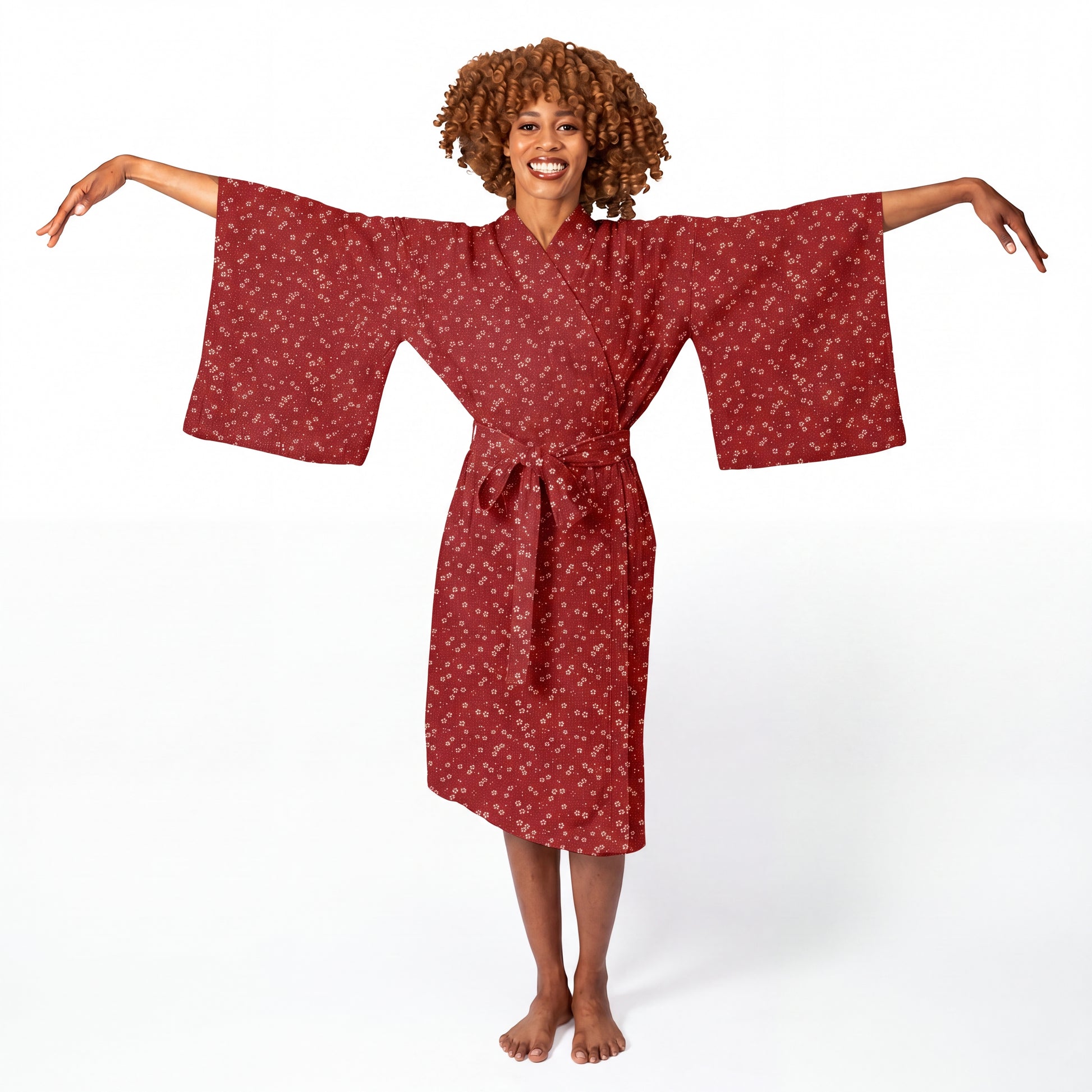 A woman modeling a red kimono-style robe with a small white floral pattern, standing against a plain white studio background with her arms outstretched.