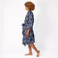 A woman with curly brown hair is shown in profile wearing a navy blue and white patterned kimono-style robe, walking barefoot against a plain white studio background.