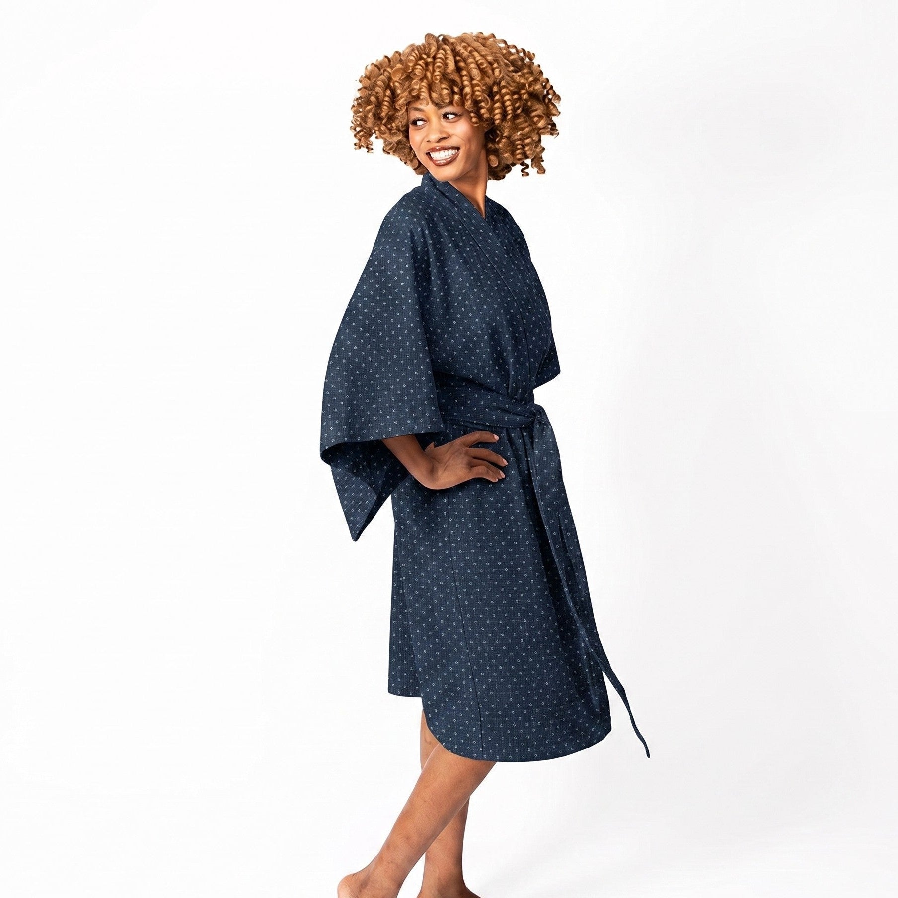 A woman modeling a dark navy blue cotton robe with a small white geometric pattern, standing barefoot against a solid white studio background.