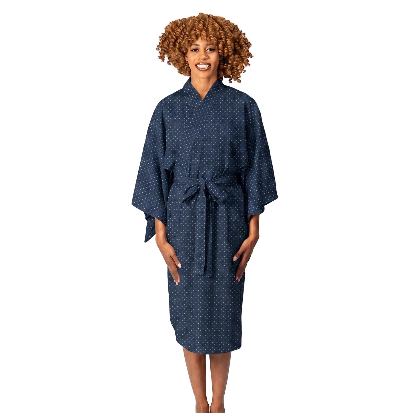 A woman with curly brown hair wearing a dark navy blue kimono robe with a small white geometric pattern, standing against a plain white studio background.