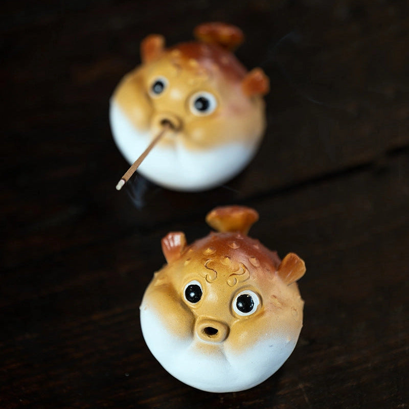Two puffer fish incense holders on a dark table.