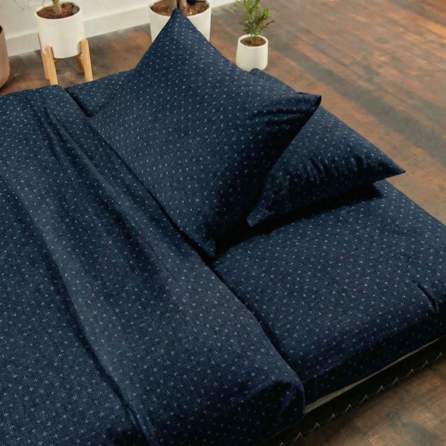 Navy blue polka dot bedding set on a bed with wooden floor and plants in the background