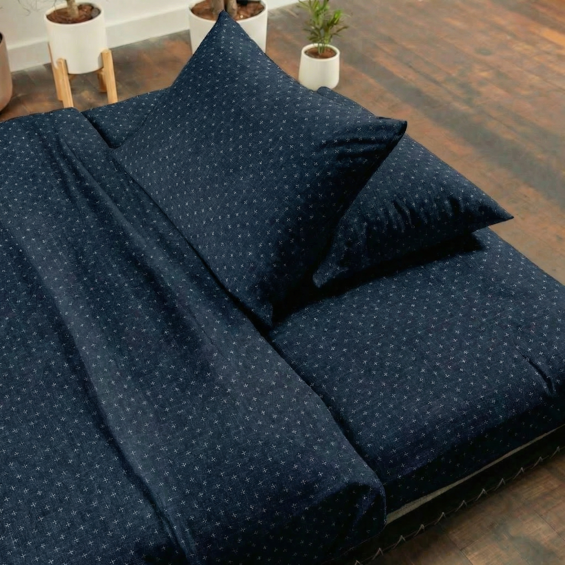 Navy blue polka dot bedding set on a bed with wooden floor and plants in the background