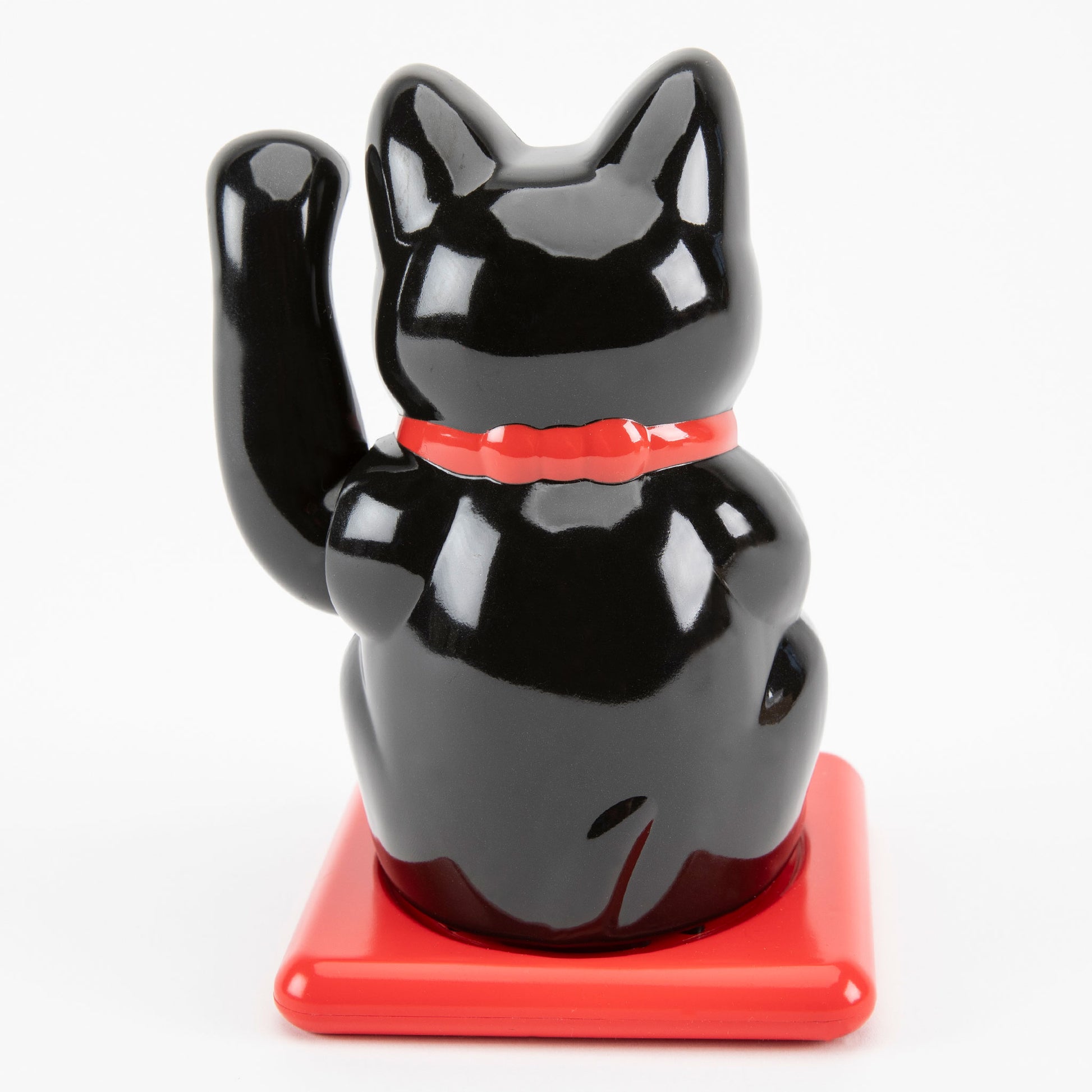 Black maneki-neko cat on a red base with a white background