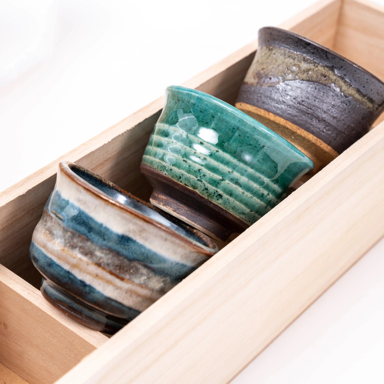 Three ceramic cups with different glaze patterns in a wooden box.
