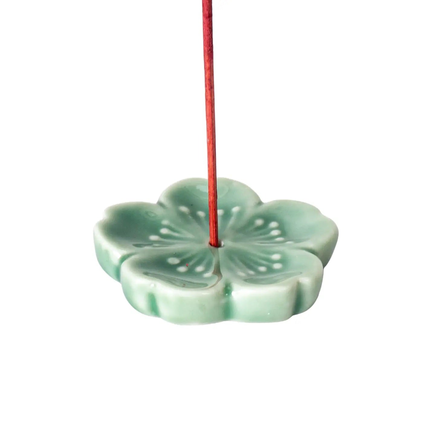 Green ceramic incense holder with a red incense stick on a white background