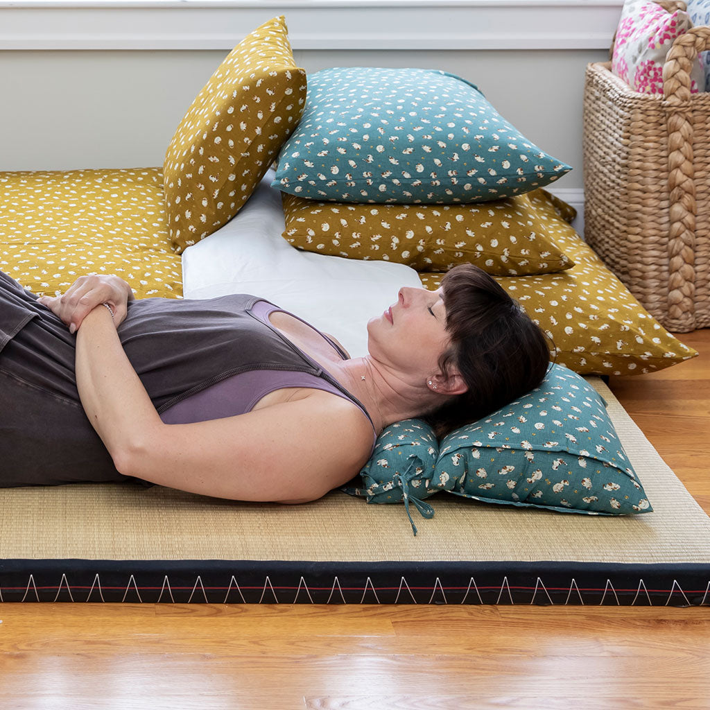 Woman lying on a mat with decorative pillows in a room setting